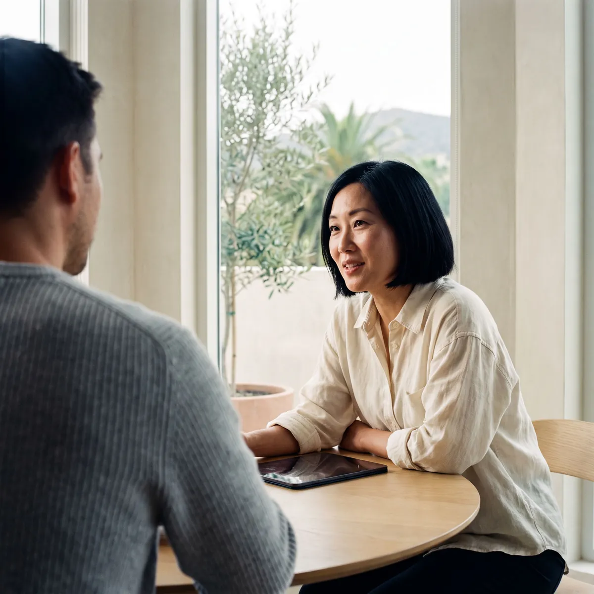 A bakery owner leaning in mid-conversation across a round table, a tablet lying between her and her advisor